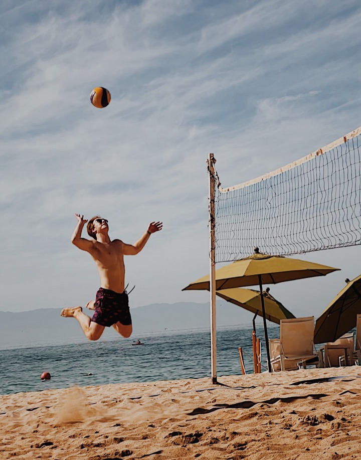 Kobey jumping to serve in beach volleyball